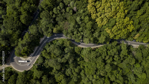 Aerial stock photo of car driving along the winding mountain pass road through the forest in Sochi, Russia. People traveling, road trip on curvy road through beautiful countryside scenery.