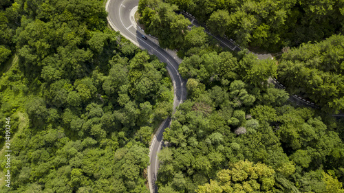 Fototapeta Naklejka Na Ścianę i Meble -  Aerial stock photo of car driving along the winding mountain pass road through the forest in Sochi, Russia. People traveling, road trip on curvy road through beautiful countryside scenery.