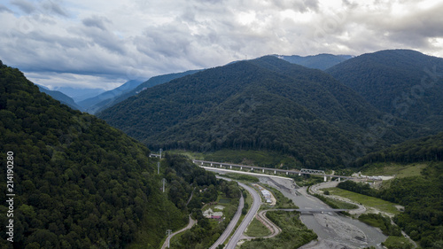 Aerial stock photo of car driving along the winding mountain pass road through the forest in Krasnodar Krai, Russia. People traveling, road trip on curvy road through beautiful countryside scenery.