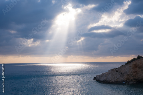 Sunray penetrating the clouds at sunset ilumminating the ocean water photo