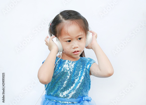 Adorable little Asian girl in bright dress listening music with headphones isolated on white background.