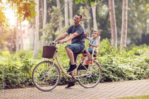 Smiling father with boy on bicycles having fun in park. Family sport and healthy lifestyle.