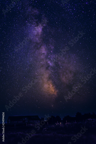 The Milky Way and stars in the night sky over the house and trees.