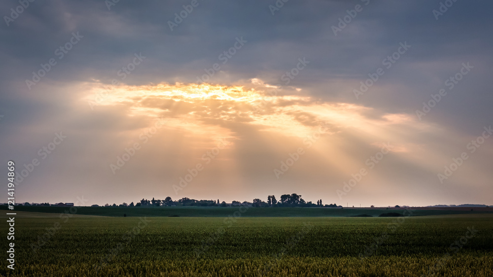 Rural landscape with dark dramatic sky during sunrise. The rays of the sun penetrate through a dark cloud