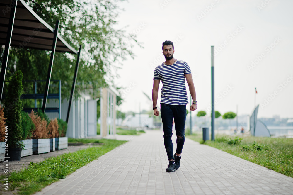 Handsome tall arabian beard man model at stripped shirt posed outdoor. Fashionable arab guy.