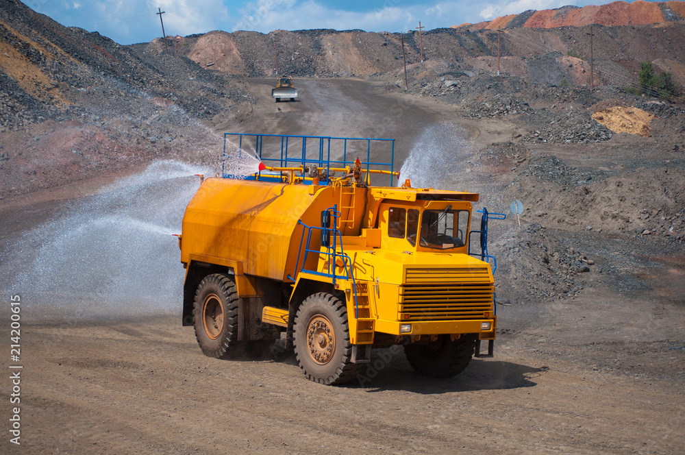 Heavy truck pours the road with water in the iron ore quarry. Dust removal, protection of the environment. Irrigation of the road from dust Heavy truck pours the road with water in the iron ore quarry. Dust removal, protection of the environment. Irrigation of the road from dust