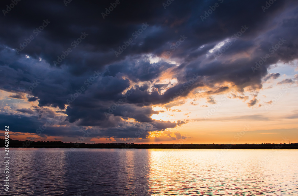 Sunset in the lake. Beautiful sunset behind the storm clouds before a thunder storm above the over lake landscape background. Dramatic sky with cloud at sunset.
