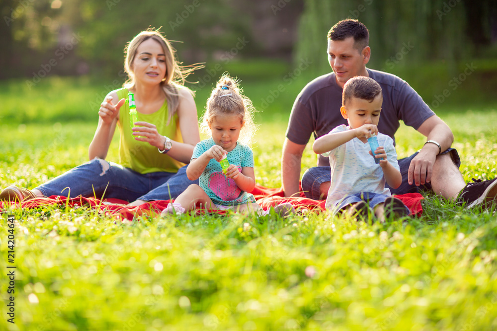 Fototapeta premium Family in park -Male and female child blow soap bubbles outdoor.