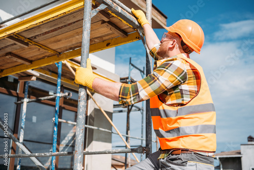 Obraz na plátně Handsome builder climbing on scaffolding at construction site
