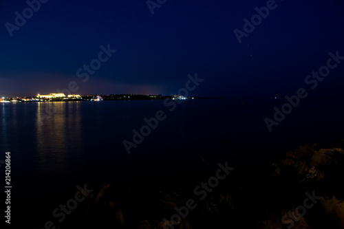 Sunset and the night light in Ravda. Bulgaria. Reflection of light of the city in the sea.