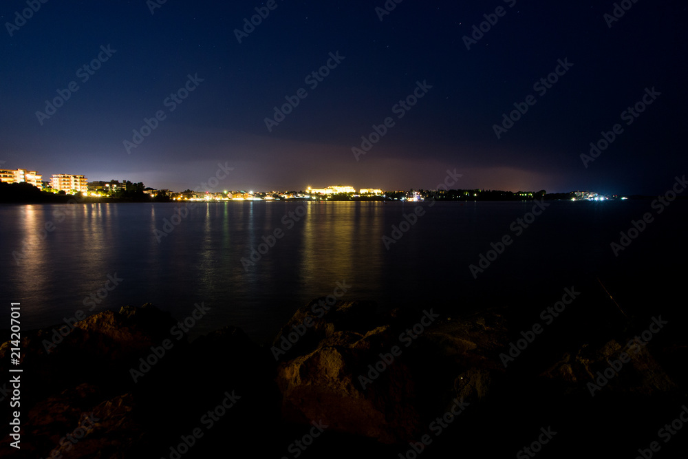 Sunset and the night light in Ravda. Bulgaria. Reflection of light of the city in the sea.