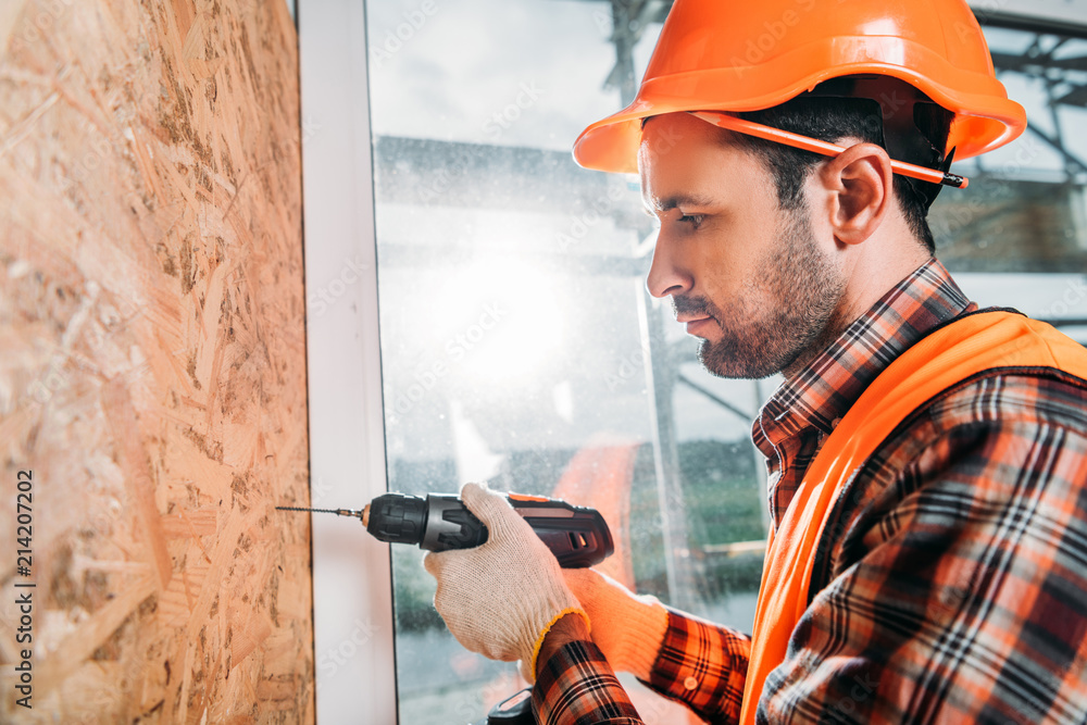 side view of handsome builder using handheld electric drill