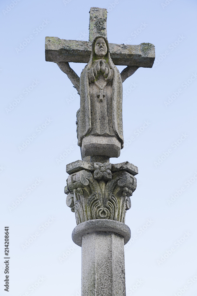Ancient white stone crucifix with Virgin Mary in blue sky