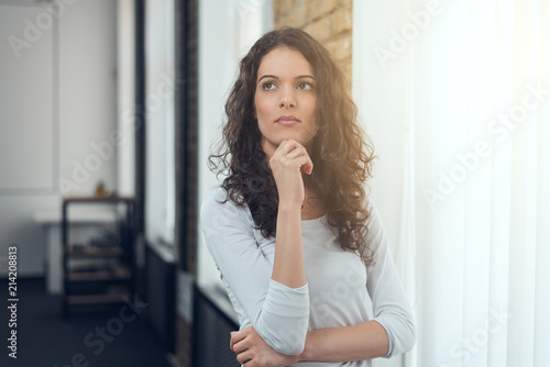 Attractive girl in casual t-shirt squeezing eyes and keeping hand on chin in doubt and suspicion, thinking about something photo