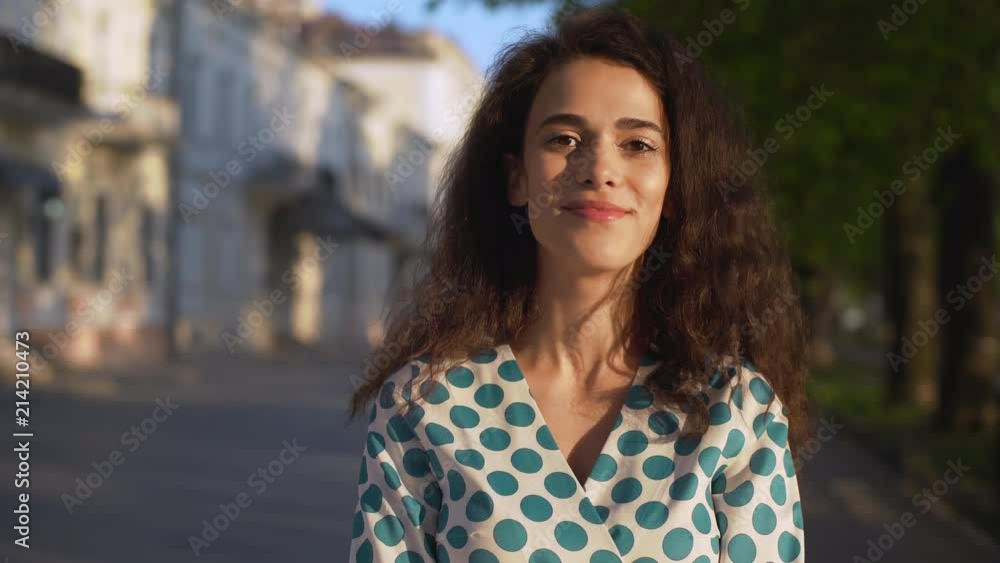 Portrait of caucasian cheerful woman wearing dress smiling, while walking through boulevard in morning Portrait of caucasian cheerful woman wearing dress smiling, while walking through boulevard in morning