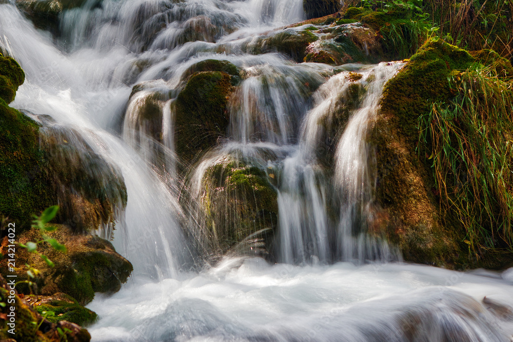 Small waterfall, water stream between rocks and grass