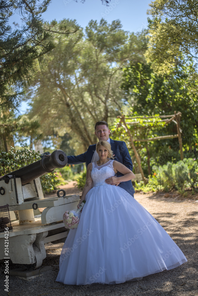 Fototapeta premium Just married couple wearing wedding dresses standing beside vintage cannon. Shot at wedding in Australia on amazing sand beach.
