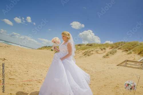 Beautiful bride wearing white wedding dress with bouquet in her hands at beach. Shot at wedding in Australia on amazing sand beach.