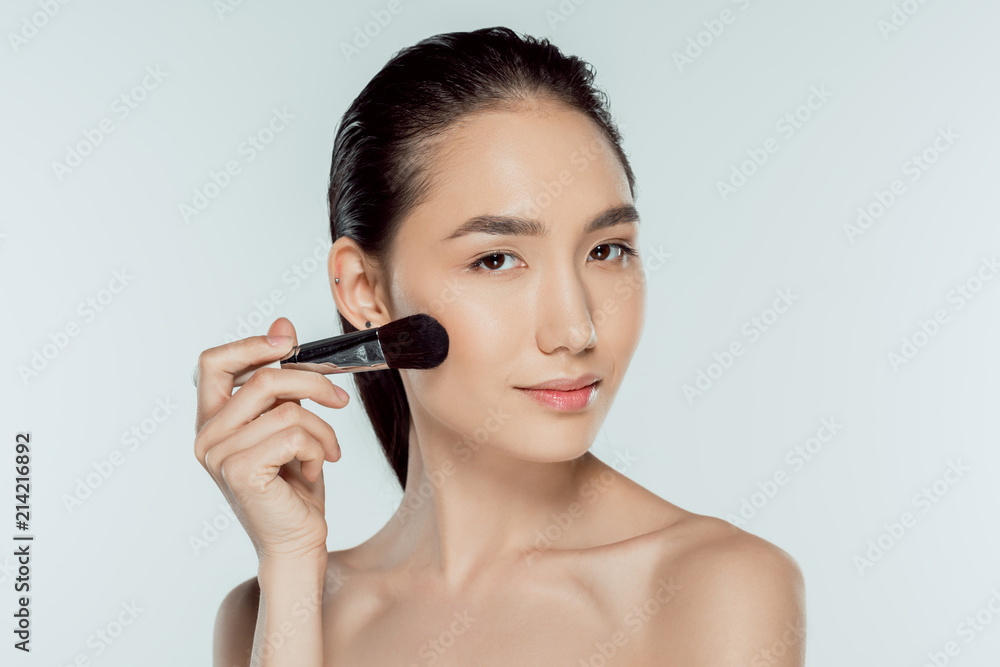 asian girl applying blushes with cosmetic brush, isolated on grey asian girl applying blushes with cosmetic brush, isolated on grey
