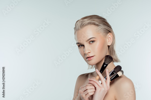 beautiful blonde girl holding makeup brushes, isolated on grey