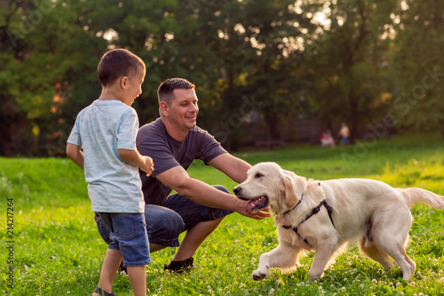 Beautiful happy family is having fun with golden retriever - Father and his son playing with dog in park.