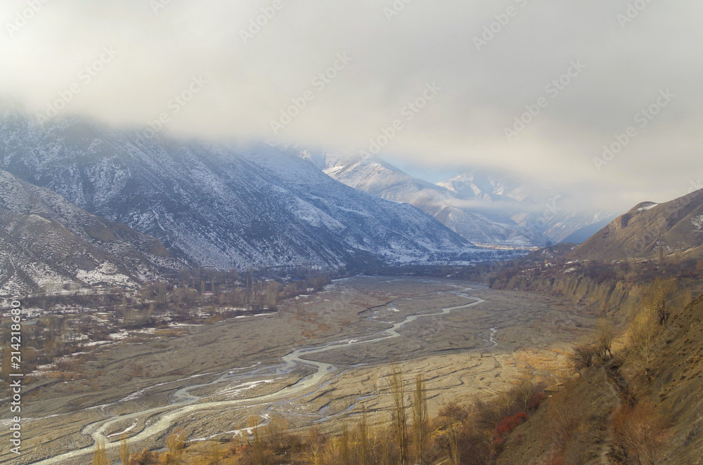 Scenic view of valley of the river Akhtychay which is filled in with sunlight. Snow-covered mountains hidden by clouds. Nature and travel. Russia, North Caucasus, Dagestan, Akhty