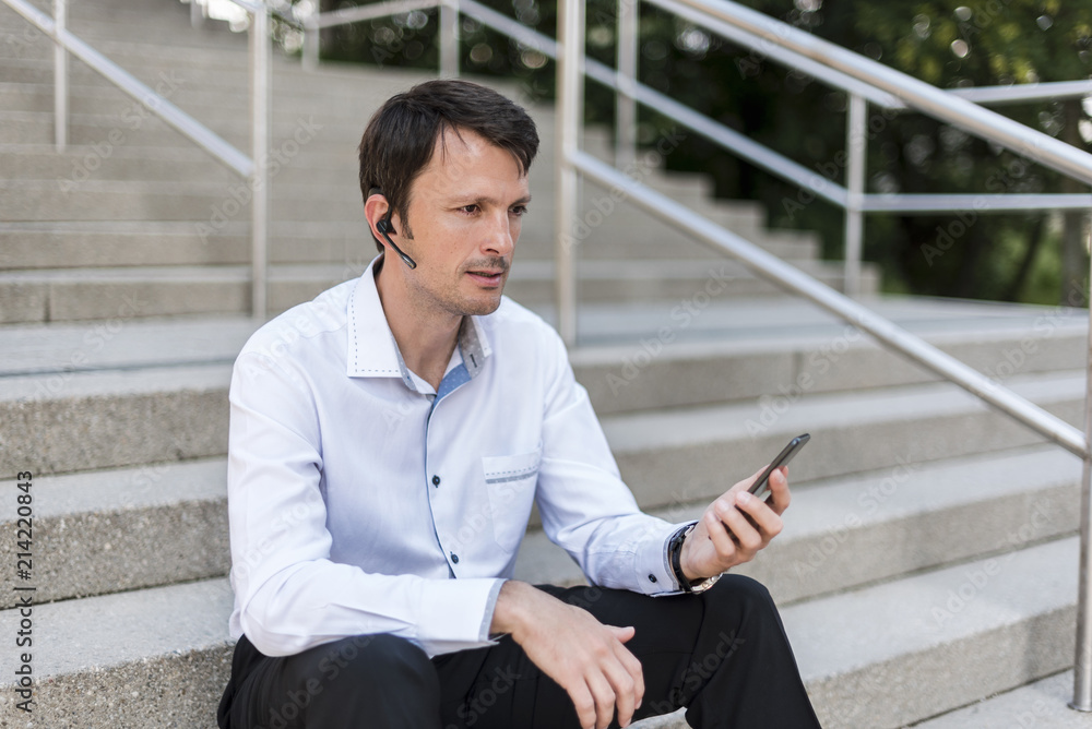 Businessman with headset and cellphone sitting on stairs Businessman with headset and cellphone sitting on stairs