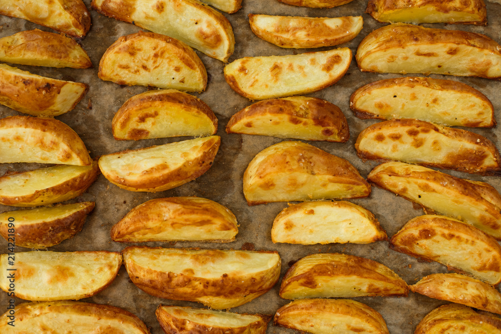 Background of rosy slices of roasted potatoes on the baking paper