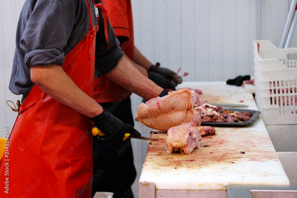 Butcher in red apron chopping chicken meat. Cutting shop of a poultry farm.
