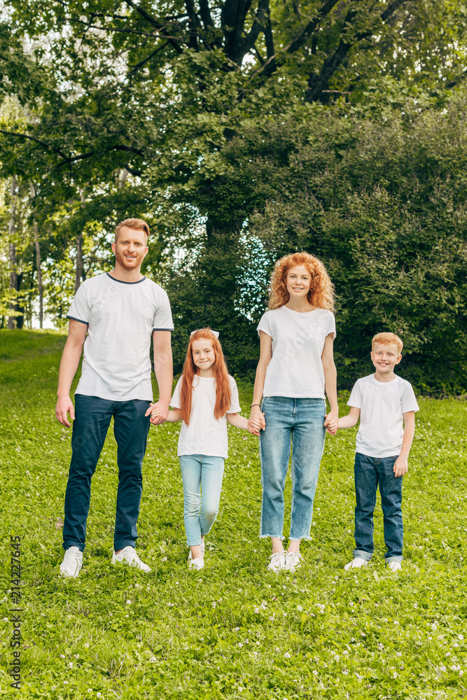 Obraz premium happy family with two kids holding hands and smiling at camera in park