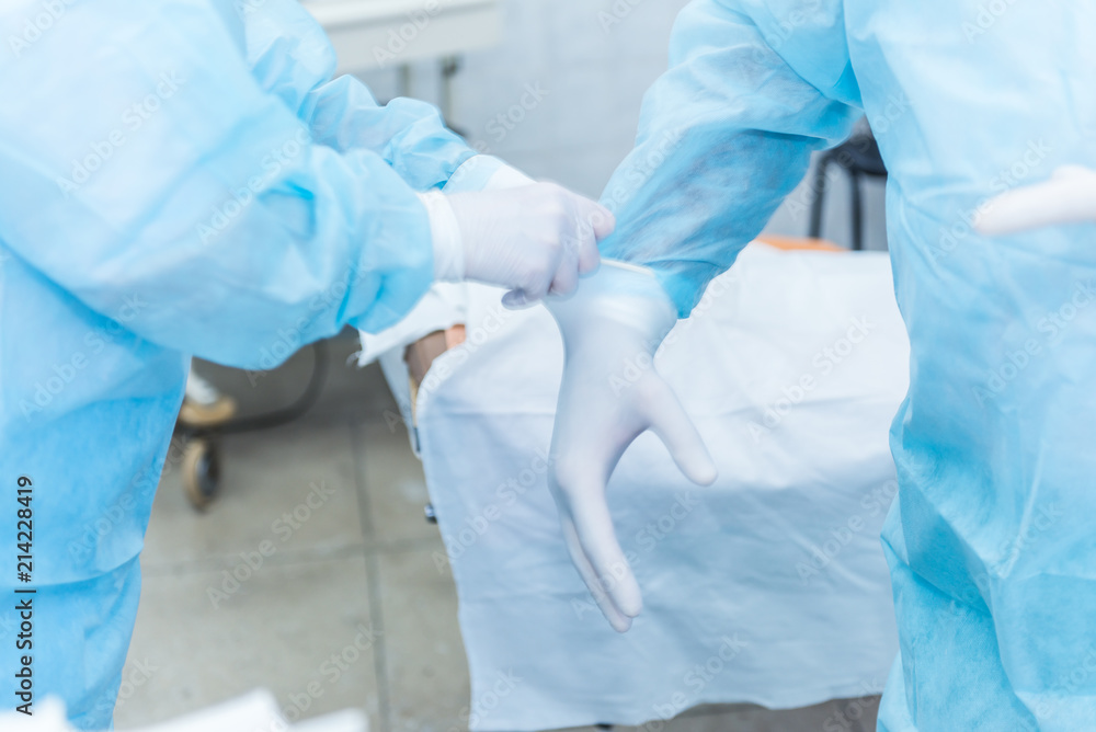 The doctor's assistant helps put the sterile latex gloves on the surgeon before surgery in the hospital The doctor's assistant helps put the sterile latex gloves on the surgeon before surgery in the hospital