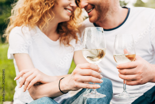 cropped shot of happy couple holding glasses of wine in park