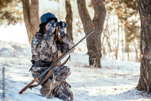 A girl hunter looks through binoculars in the woods, looks out for prey. The concept of modern hunting, equipment