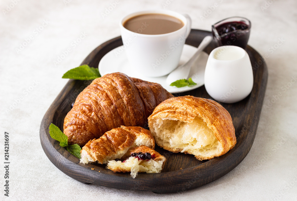 Breakfast concept: two fresh french croissant with a cup of coffee and jam on a dark wooden tray. Breakfast concept: two fresh french croissant with a cup of coffee and jam on a dark wooden tray.