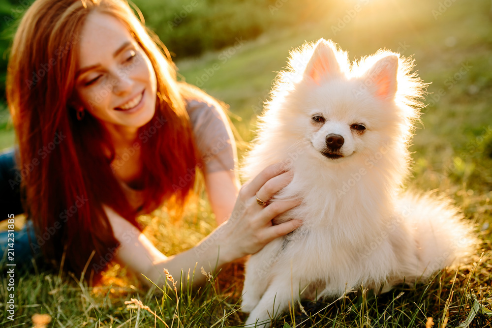 The cute red-haired woman in a hat with a spitz-dog in the park. Beautiful sunset light. Background toning for instagram filter. The cute red-haired woman in a hat with a spitz-dog in the park. Beautiful sunset light. Background toning for instagram filter.