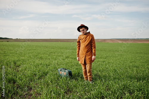 Stylish man in glasses, brown jacket and hat with bag posed on green field. © AS Photo Family