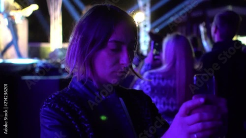 Woman using mobile phone taking selfie photo on open air live festival night show concert with blurry stage as background