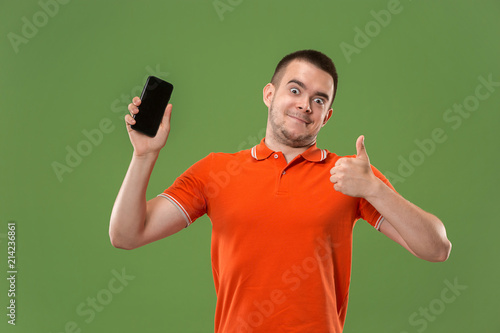 The happy man showing at empty screen of mobile phone against green background.