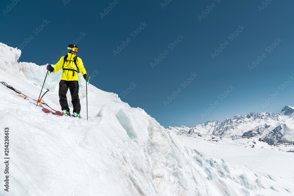 A freerider skier in complete outfit stands on a glacier in the North Caucasus against the background of the Caucasian snow-capped mountains