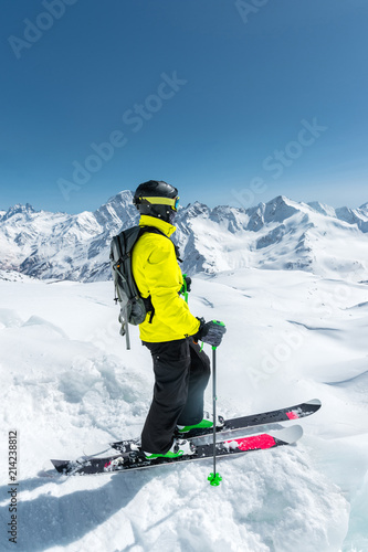 A freerider skier in complete outfit stands on a glacier in the North Caucasus against the background of the Caucasian snow-capped mountains