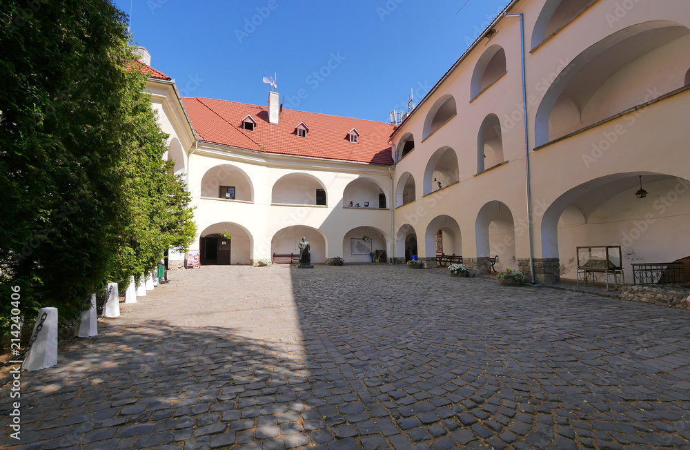 The courtyard of the building is paved with cobblestone with growing trees and a small monument
