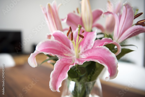Fototapeta Naklejka Na Ścianę i Meble -  Bouquet pink lily flowers in glass vase on wood table in room.