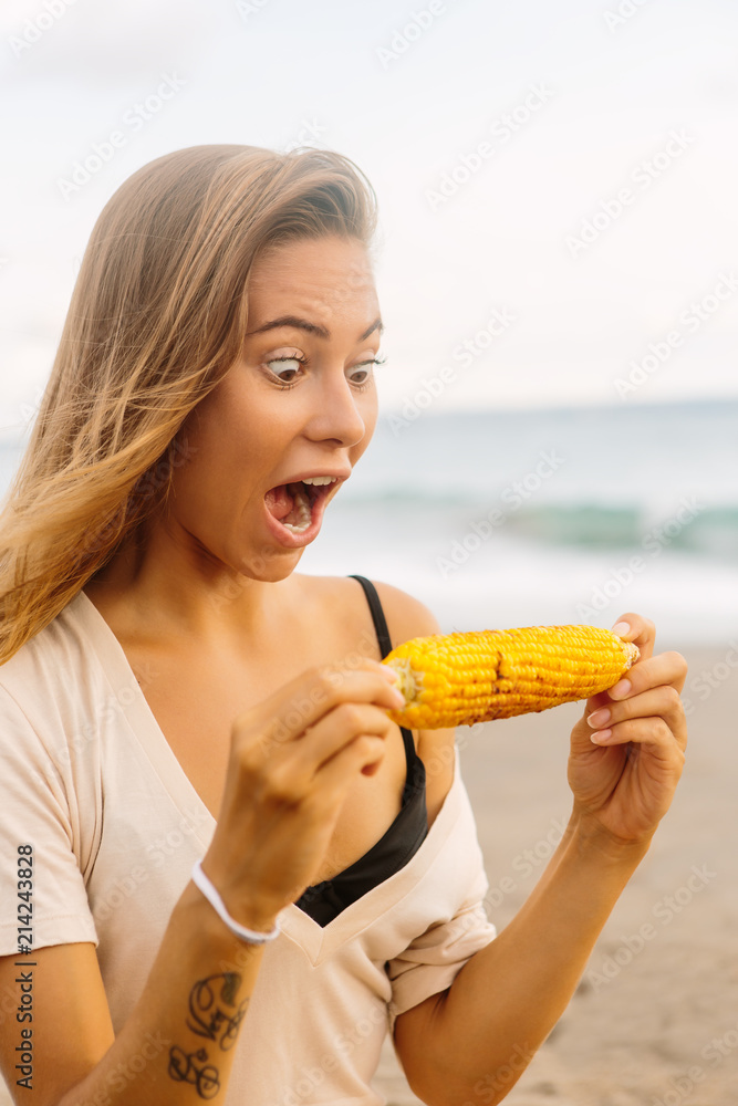 Pretty vegetarian hipster woman in summer casual outfit with healthy fresh grilled corn. Sexy lady on sea beach sunset or ocean sunrise. Travel, explore, active yoga and meditation lifestyle concept. Pretty vegetarian hipster woman in summer casual outfit with healthy fresh grilled corn. Sexy lady on sea beach sunset or ocean sunrise. Travel, explore, active yoga and meditation lifestyle concept.