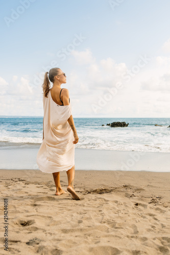 Pretty girl in casual clothes and wooden sunglasses stay on the hot sand. Beautiful lady on sea exotic beach sunset or ocean sunrise. Travel, explore, active yoga and meditation lifestyle concept. © Mikalai Bachkou