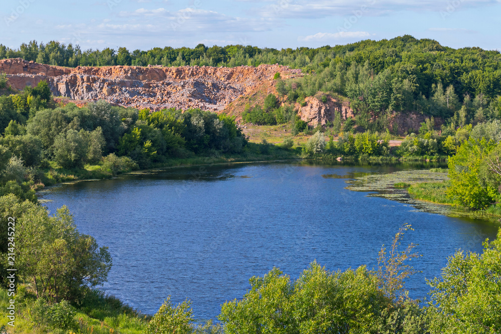 Blue pond in the foreground and quarry of bright red color in the background