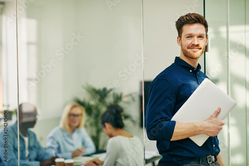 Smiling young businessman standing with his laptop in an office