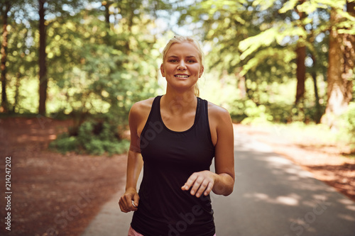 Smiling young blonde woman jogging alone along a forest path