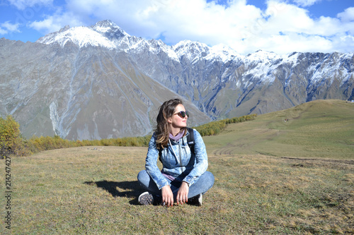 Woman sitting on grass at mountains on background, Kazbegi, Georgia