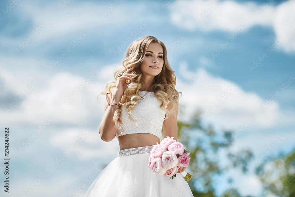 Beautiful and sensual blonde model girl with sexy body in stylish tulle skirt and in fashionable blouse adjusting her hairstyle and posing outdoors at the park Beautiful and sensual blonde model girl with sexy body in stylish tulle skirt and in fashionable blouse adjusting her hairstyle and posing outdoors at the park