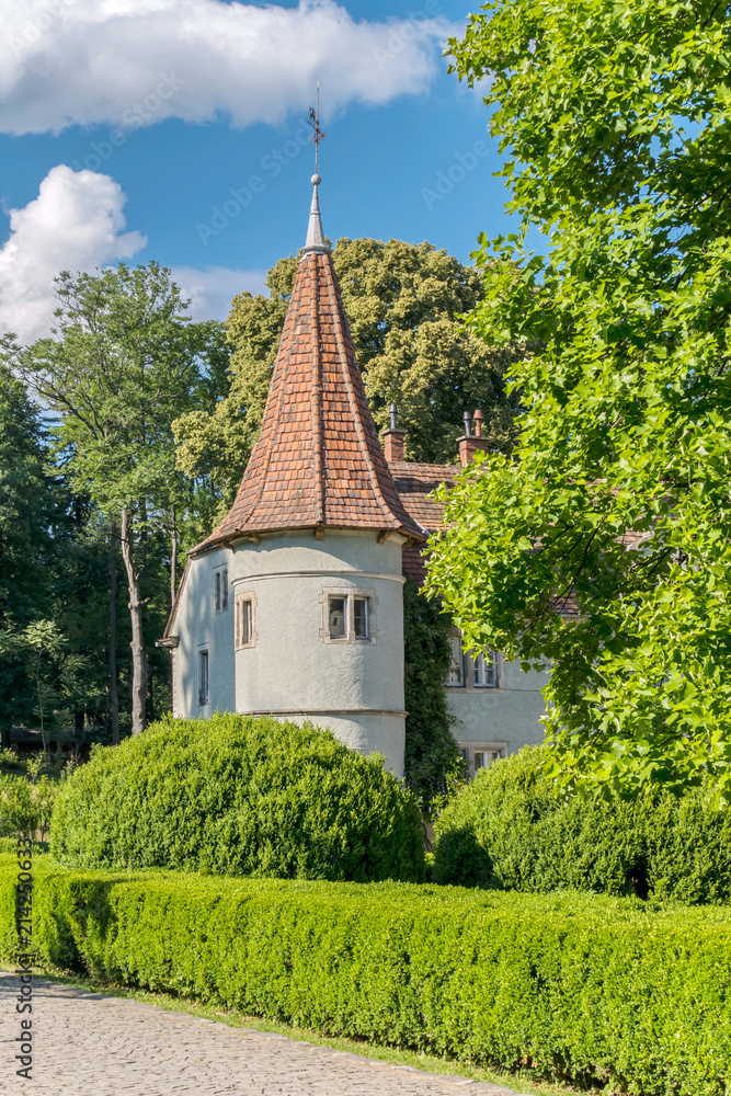 A low tower of the castle with a red roof and slit against the background of green trees and blue sky